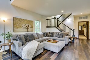 A modern living room with a sectional sofa, a decorative tree painting, a staircase, and a view of the outdoors.