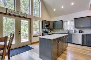 A modern kitchen with a central island, dark cabinetry, and large windows.