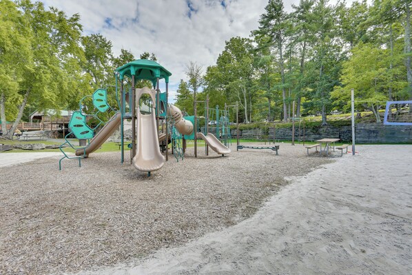 A playground with slides and climbing structures, surrounded by trees and picnic tables.