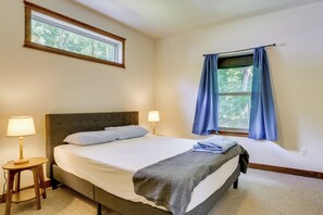 Ein Schlafzimmer mit einem Bett, Nachttischlampen, einem Fenster mit Vorhängen und Blick auf Bäume.