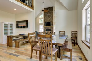 Ampla sala de jantar com uma grande mesa de madeira, várias cadeiras e uma lareira embutida.