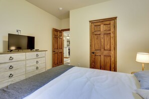A bedroom with a bed, a dresser, a television, and two wooden doors.