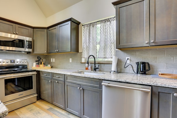 Cozinha moderna com eletrodomésticos de aço inoxidável, bancada de granito e janela com cortinas estampadas.