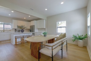 A modern kitchen with white cabinetry, a wooden island with bar stools, and a dining area with a bench and table.