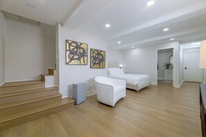 A modern hotel room with a staircase, two beds, artwork on the wall, and a ceiling with recessed lighting.