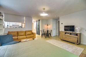 Ein modernes Wohnzimmer mit einer Couch, einem Esstisch mit Stühlen, einem Fernseher auf einer Holzkommode und einer Deckenleuchte.