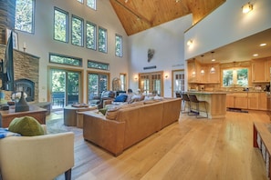 A spacious living area with a large sofa, a fireplace, and a view of the outdoors through multiple windows.