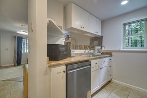 A kitchen with white cabinets, a dishwasher, a microwave, and a window with a view of trees.