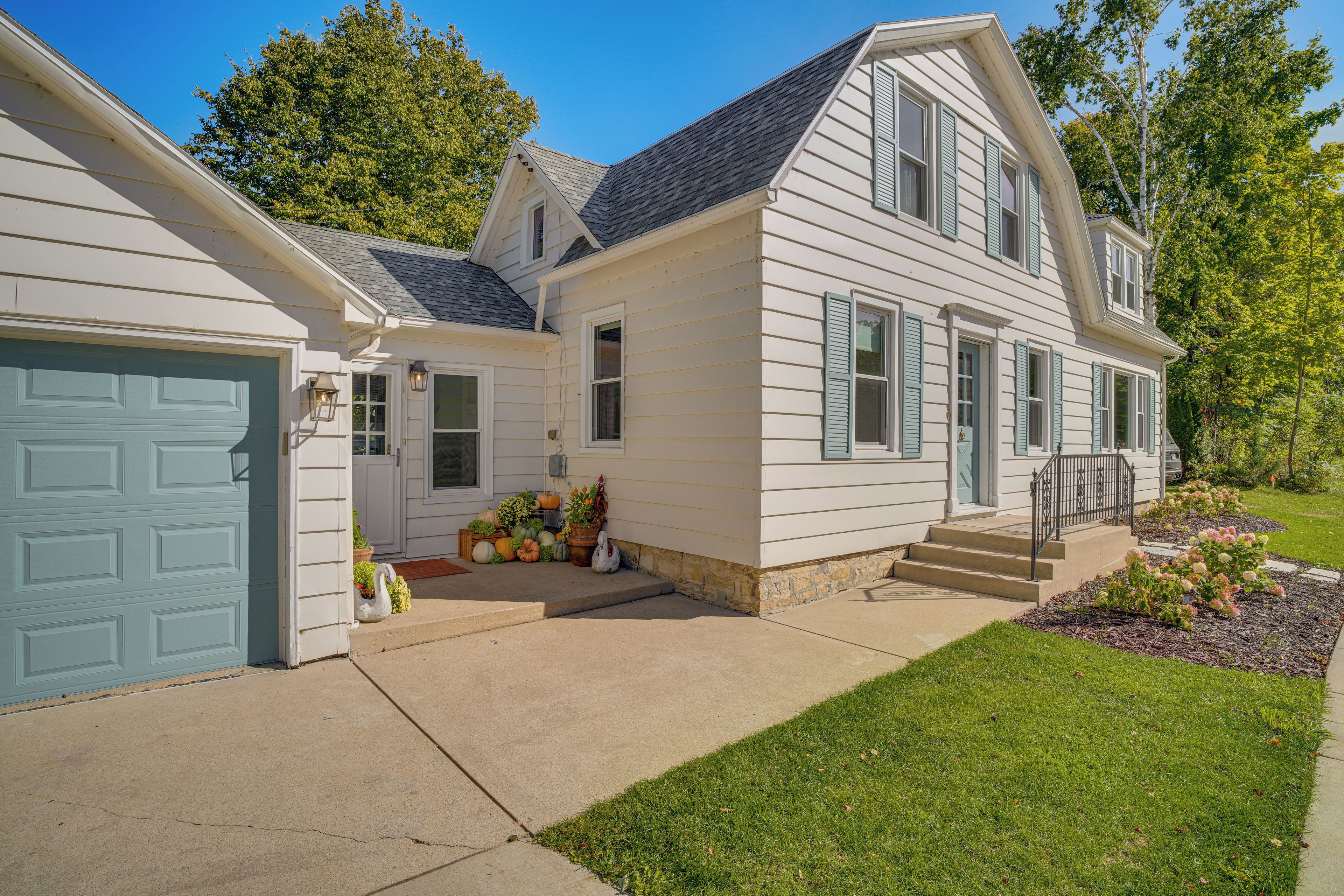 A two-story house with a garage, a front porch with potted plants, and a well-maintained lawn.