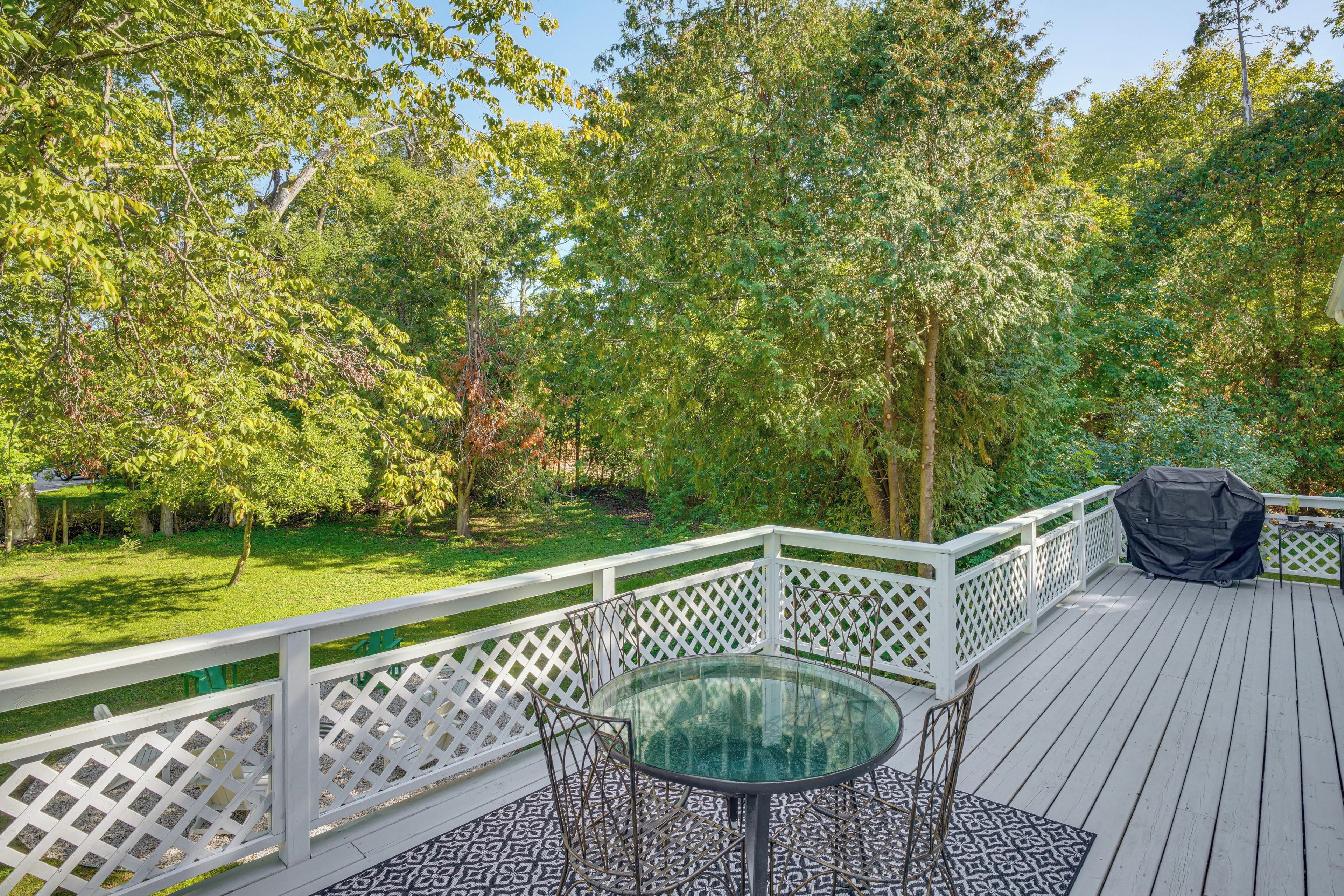 Eine Terrasse mit einem Glastisch und Stühlen, umgeben von einem weißen Gittergeländer, vor einer Kulisse aus üppigem Grün und Bäumen.