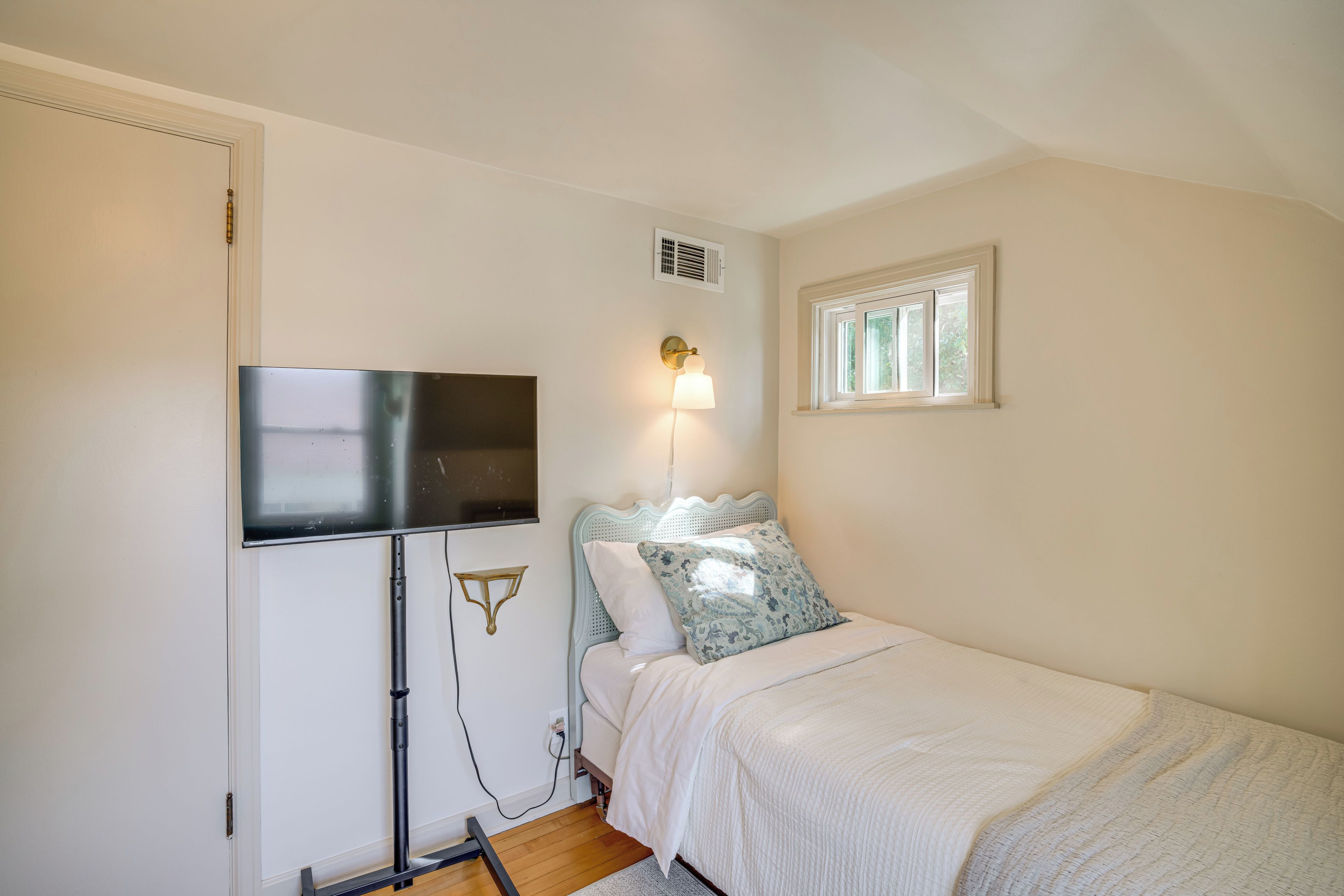 A bedroom with a bed, a television mounted on the wall, a bedside lamp, and a window.