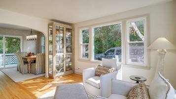 A spacious living area with a dining table, cushioned seating, and large windows offering a view of the outdoors.
