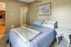A bedroom with a bed, a bedside table, a painting on the wall, and a door leading to another room.