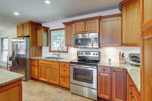 A kitchen with wooden cabinets, stainless steel appliances, a granite countertop, and a window with a view of trees.