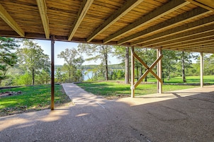 A covered outdoor area with a gravel path leading to a bench, surrounded by trees and a view of a lake.