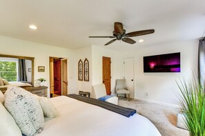Une chambre à coucher avec un lit, une chaise, un ventilateur de plafond, un téléviseur et une fenêtre avec des rideaux.