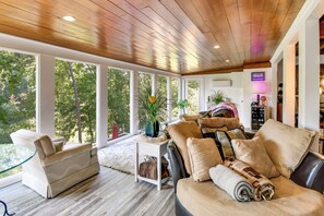 A cozy living room with a wooden ceiling, large windows, a sofa, and a chair. - Game & Theater Rooms! Lake Hartwell Family Oasis (Lavonia)