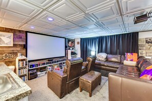 A home theater room with a large flat-screen TV, leather seating, and a bookshelf filled with DVDs. - Game & Theater Rooms! Lake Hartwell Family Oasis (Lavonia)