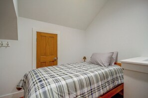 A small, single-bed room with a wooden door, a bedside table with a lamp, and a plain white wall. - Play & Unwind! Pass Christian Home < 1 Mi to Gulf (Pass Christian)