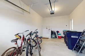 Un grand espace intérieur où sont rangés des vélos le long du mur, un coin douche avec un tuyau d’arrosage, et un meuble de rangement bleu portant l’inscription « casela ».