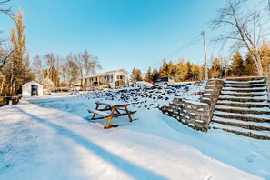 A snow-covered outdoor area with a picnic table, a stone wall, and a house in the background.