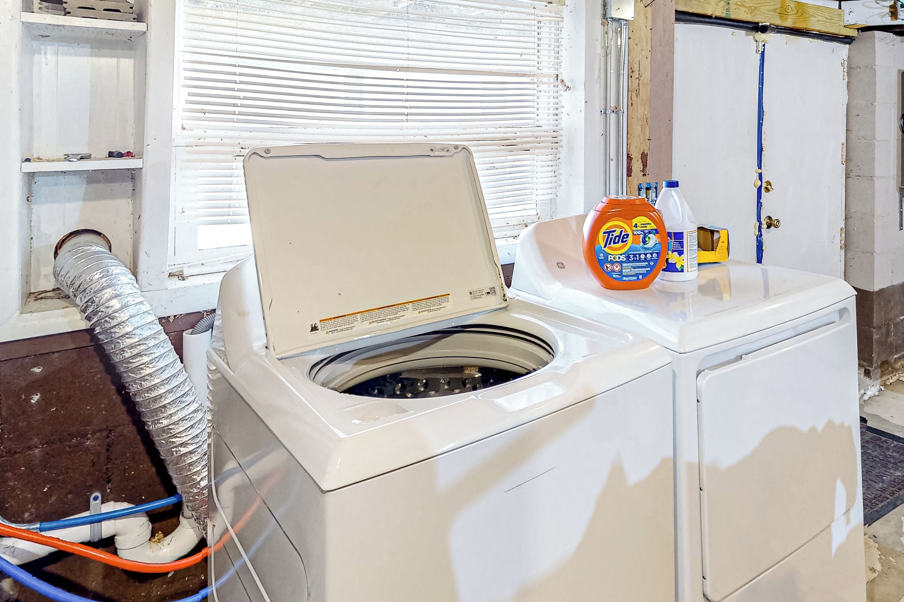 A white washing machine with a lid open, a bottle of Tide detergent, and a hose connected to it.