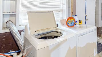 A white washing machine with a lid open, a bottle of Tide detergent, and a hose connected to it.