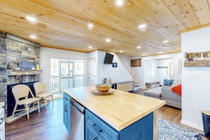 A spacious kitchen with a large island, wooden ceiling, stone wall, and a stone fireplace.
