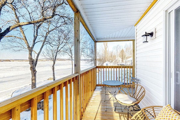 A covered porch with a wooden railing, a table with chairs, and a view of a snowy landscape. - Waterfront Escape on Long Lake! Ski, Paddle + Play (Saint David)