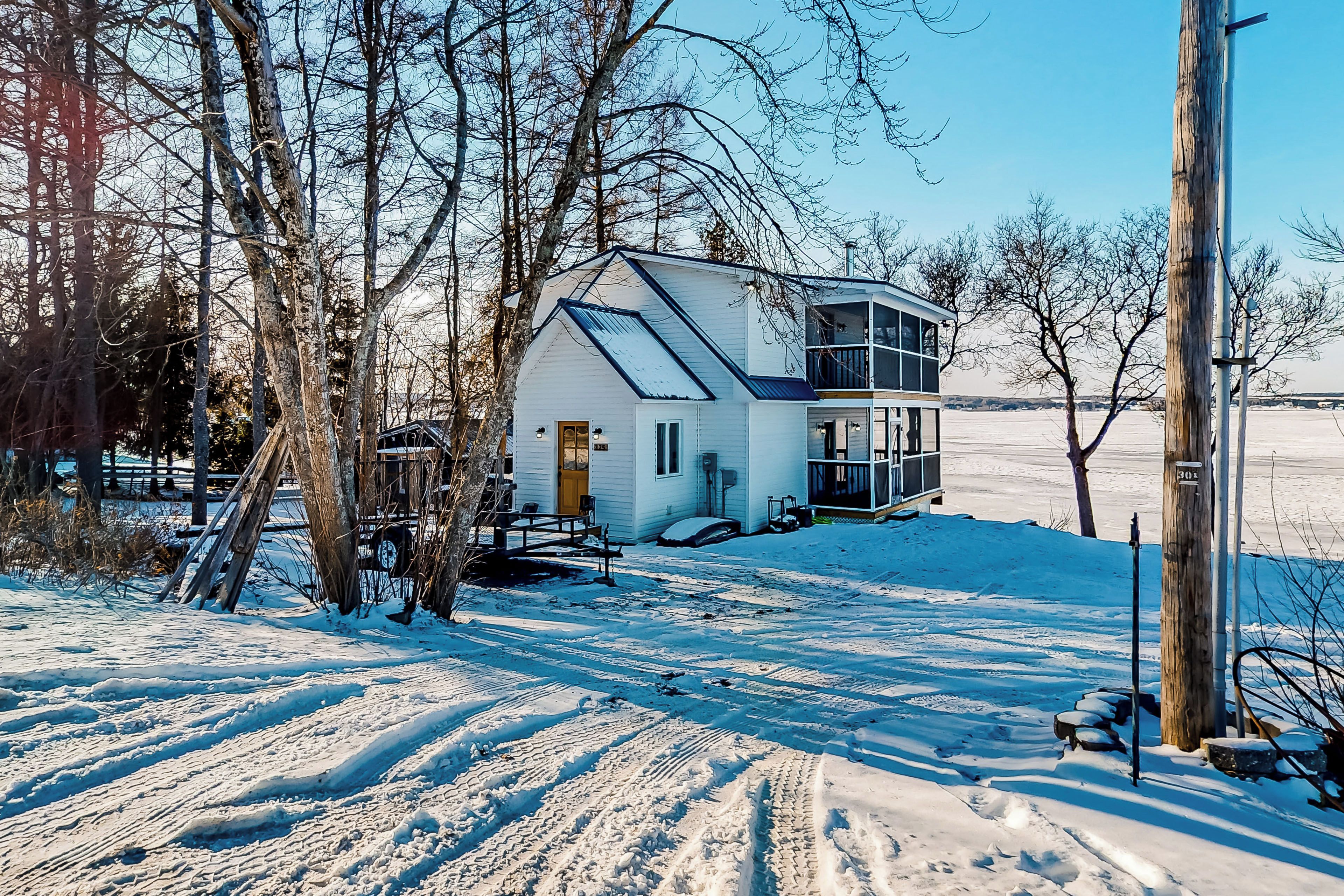 A snow-covered landscape with a two-story house featuring a large window and a balcony.