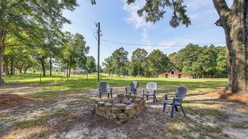 A fire pit with chairs in a grassy area with trees and a barn in the background.