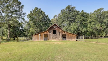 A rustic wooden barn with a star on the roof, surrounded by a fenced pasture and tall trees.