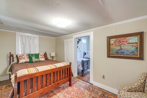 A bedroom with a wooden bed, a patterned rug, a painting, and a door leading to another room.