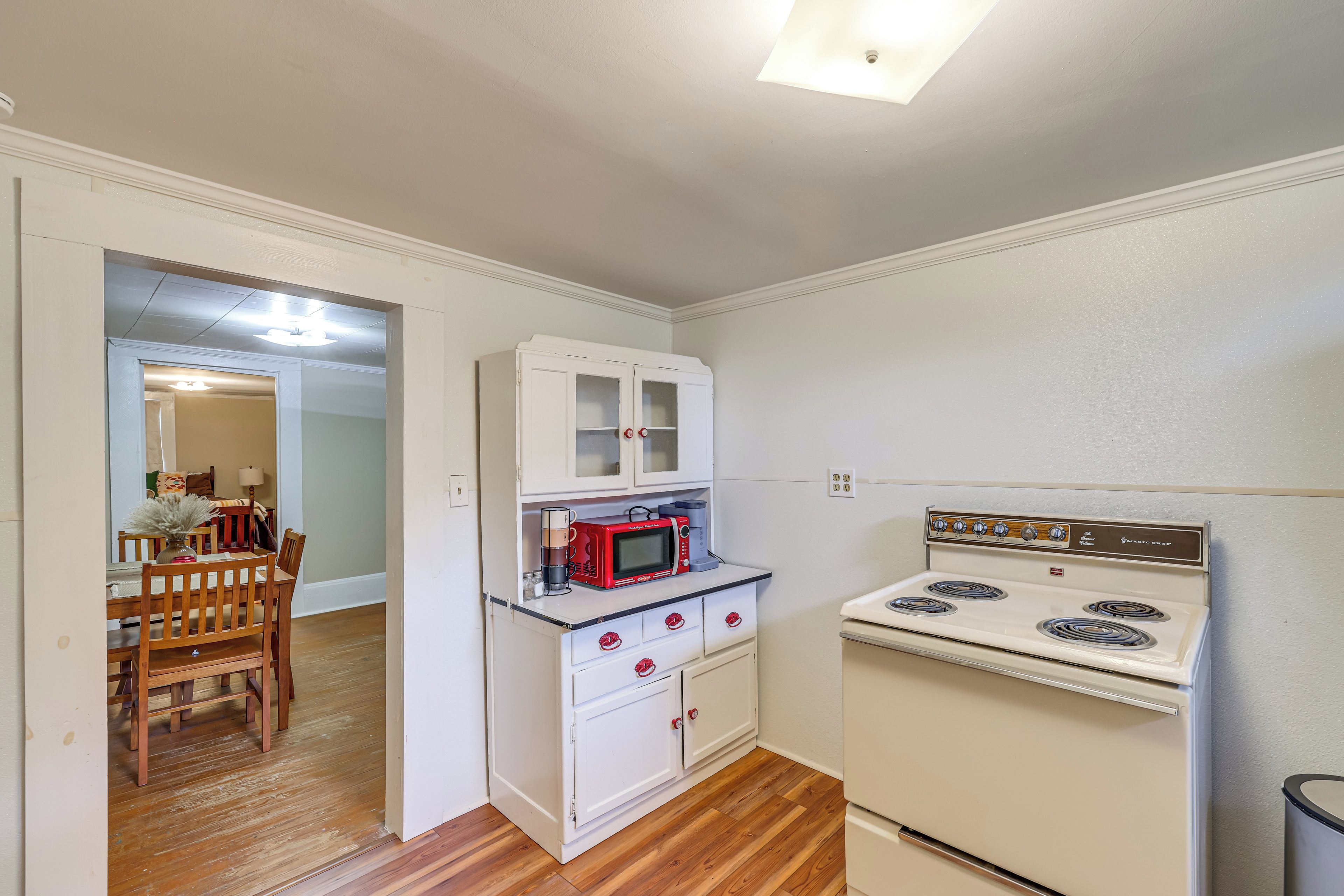 Une cuisine de taille réduite avec des meubles blancs, un micro-ondes rouge et une cuisinière blanche.