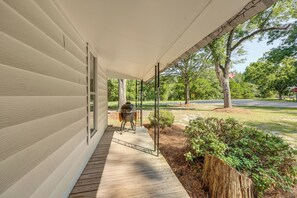 A covered porch with a grill, a wooden deck, and a view of a road and trees.