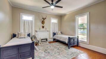 A bedroom with two beds, a ceiling fan, a fireplace, and a large window.