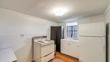 A compact kitchen with white appliances, a wooden floor, and a window with curtains.