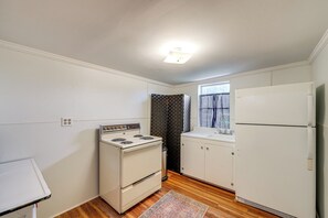 Une cuisine de taille réduite, avec des appareils électroménagers blancs, un plancher en bois et une fenêtre agrémentée de rideaux.