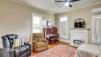 A room with a ceiling fan, a fireplace, a television, and a piano.