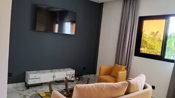 Una sala moderna con un sofá, una mesa de centro, un televisor montado en la pared y un ventanal con vistas a zonas verdes.