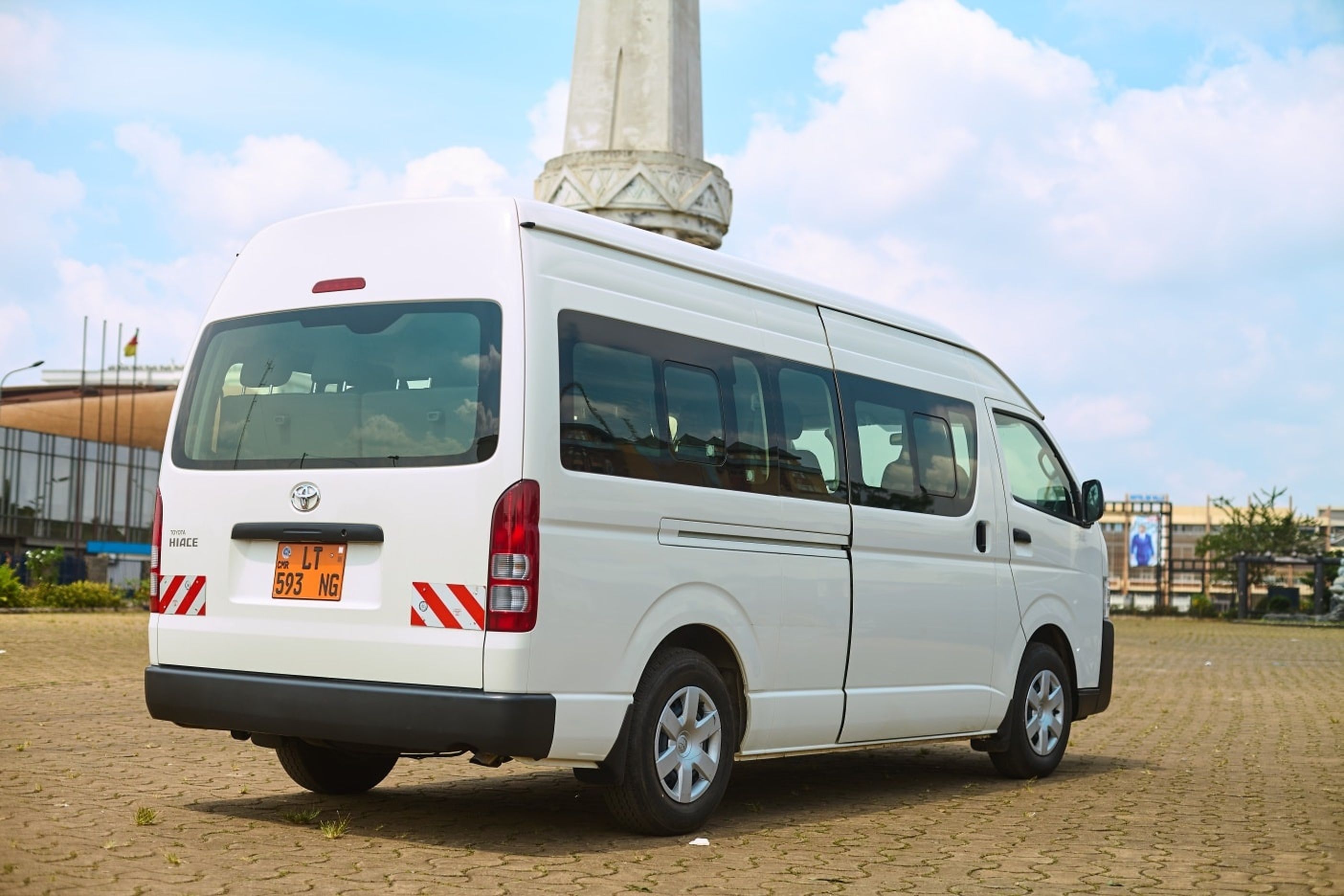 Een witte bestelwagen geparkeerd op een verhard gebied, met een monument op de achtergrond.