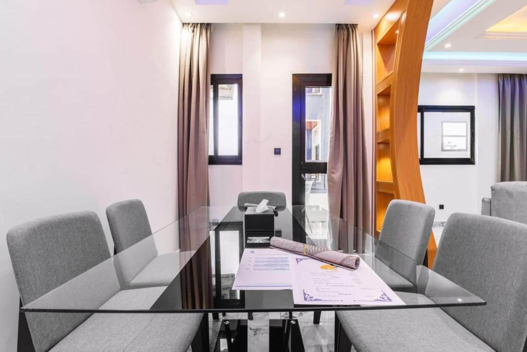 Un salón de conferencias con una mesa de vidrio, sillas grises y una pared de acento de madera.