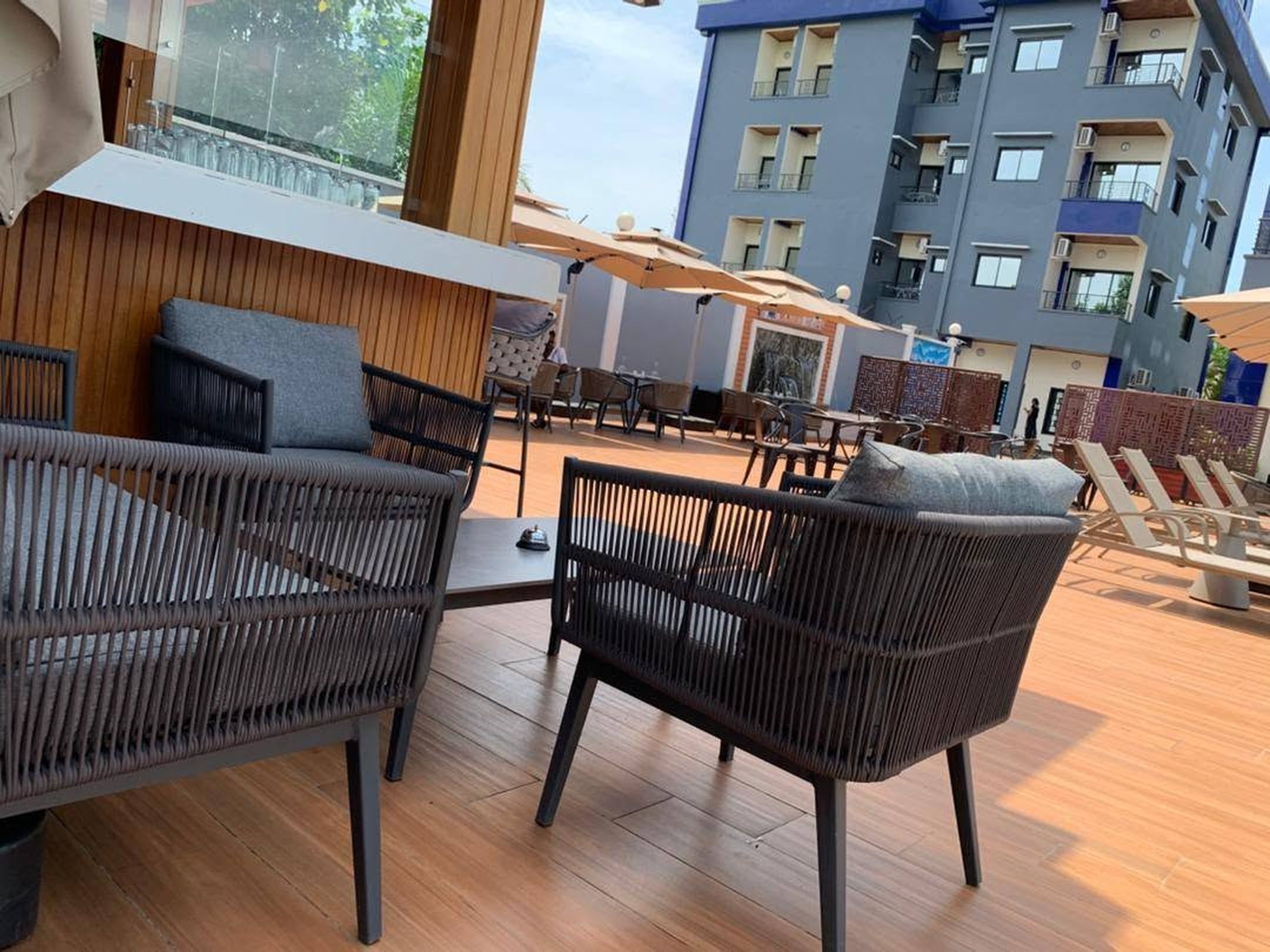 Eine Dachterrasse mit Korbmöbeln, Sonnenschirmen und Blick auf ein modernes Gebäude.