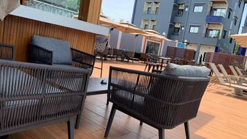 Eine Dachterrasse mit Korbmöbeln, Sonnenschirmen und Blick auf ein modernes Gebäude.