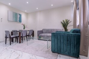 Una sala de estar moderna con una mesa de centro de vidrio, un sofá gris, un sillón color turquesa y un comedor con sillas y una mesa.