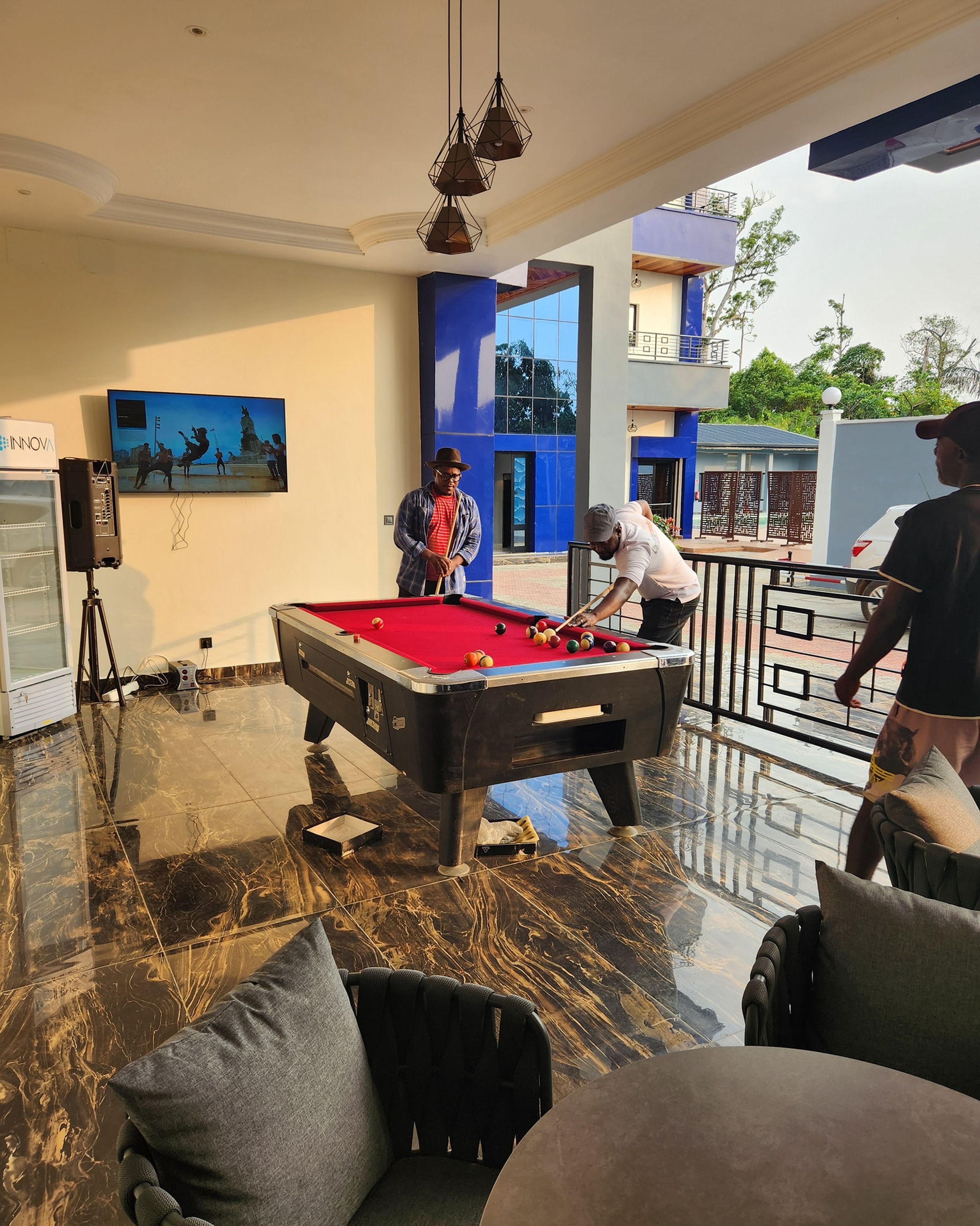 Une table de billard dans une pièce dont le sol est en marbre, un tableau au mur et un balcon donnant sur un paysage verdoyant.