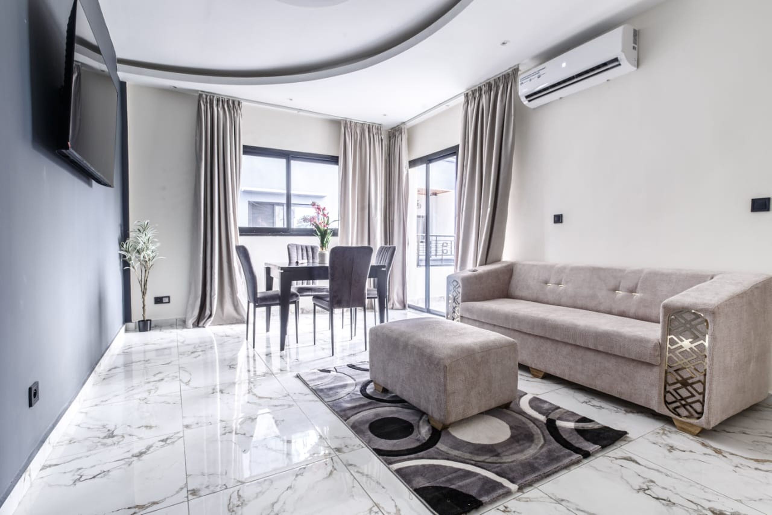 Een moderne woonkamer met een bank, poef en een eethoek met stoelen en een tafel.