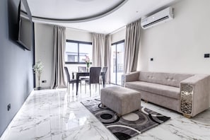Una sala de estar moderna con un sofá, un reposapiés y una zona de comedor con sillas y una mesa.