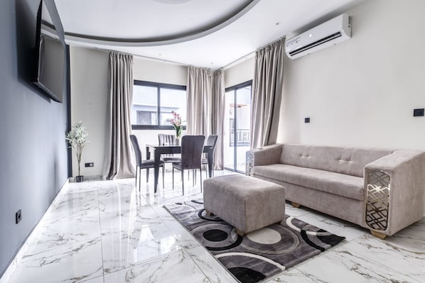 A modern living room with a sofa, ottoman, and a dining area with chairs and a table.