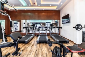 Un gimnasio con cintas de correr, máquinas de pesas y un espejo.